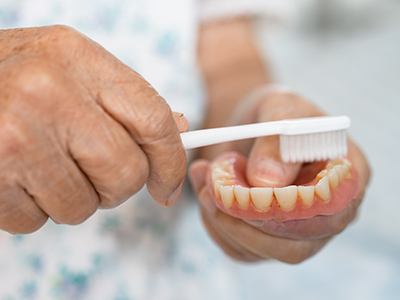 Patient using toothbrush to clean dentures