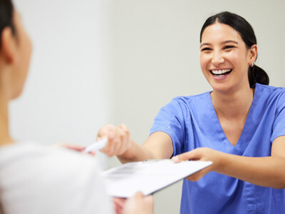 Dental assistant smiling while handing patient form