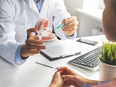 Dentist pointing to model of teeth in office with patient